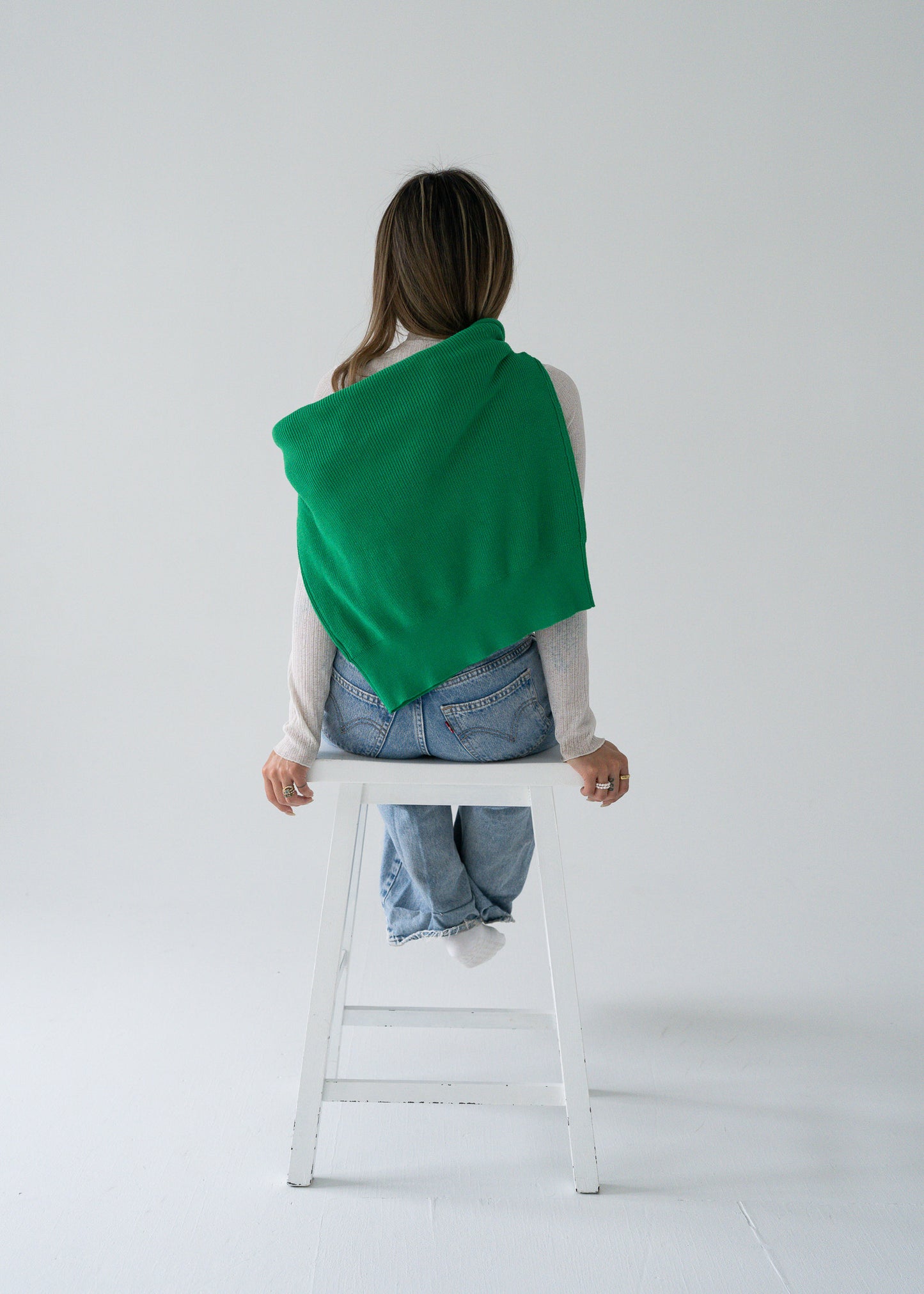 Person wearing a vintage bright parakeet green open collar knit long sleeve pullover sweater sitting on a white stool against a white background.