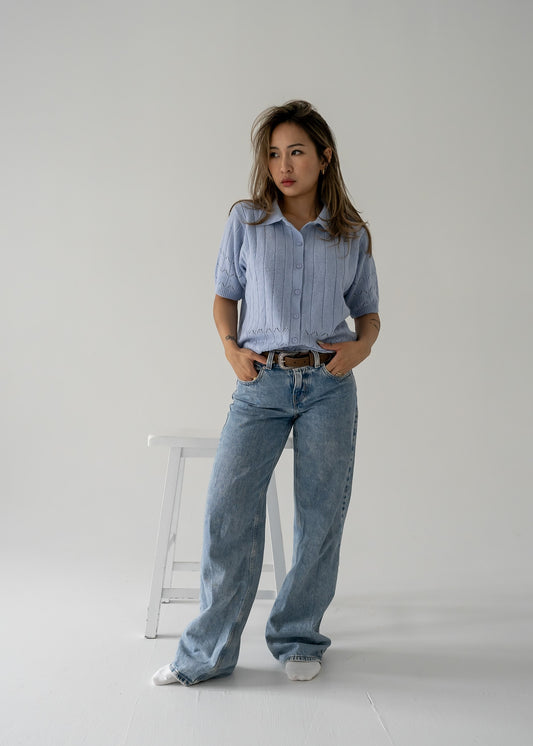 A person wearing a vintage pale lavender vertical knit collared button-up short sleeve cropped sweater paired with blue jeans, standing against a plain background.