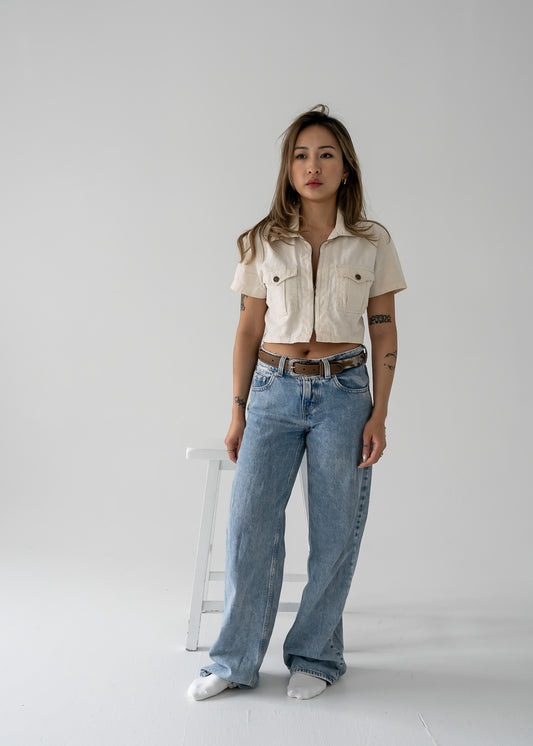 woman wearing a vintage beige cropped linen zip-up collared short sleeve jacket style top and blue jeans