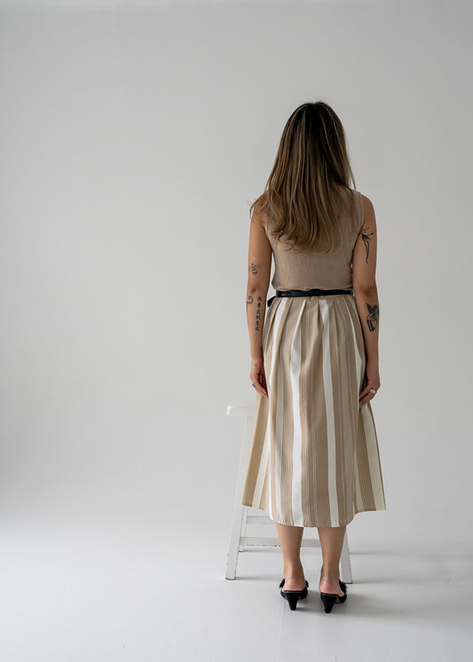 A person wearing a beige stretchy mock neck sleeveless tank top paired with a midi skirt and black shoes.