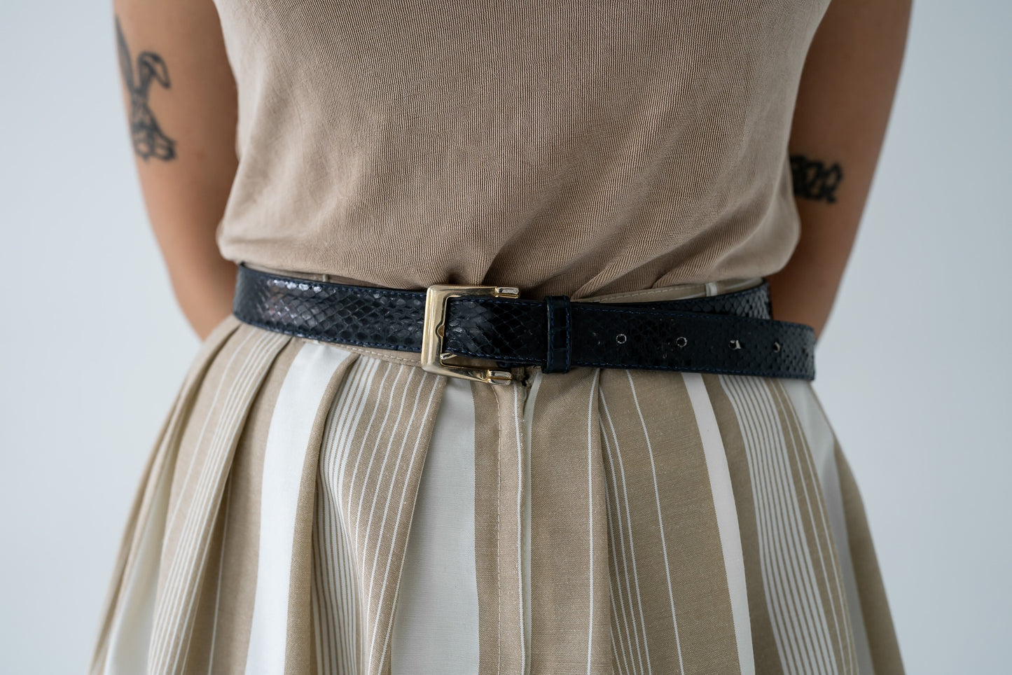 Vintage midnight navy blue snakeskin belt with gold tone buckle, displayed on a person wearing a beige skirt and a beige top.