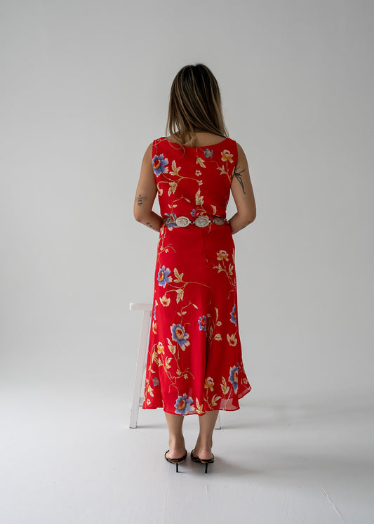 A woman wearing a bright red cowl neck bias cut floral summer dress back view