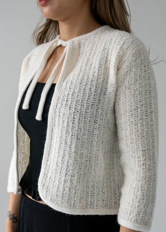 A person wearing a vintage off white cream cropped tie neck 3/4 length sleeve plush knit cardigan paired with a black outfit.