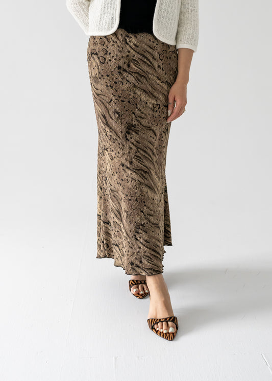 A model wearing a vintage bronze and black abstract animal print stretch scallop bottom maxi skirt with a banded elastic waist and a lettuce hem.