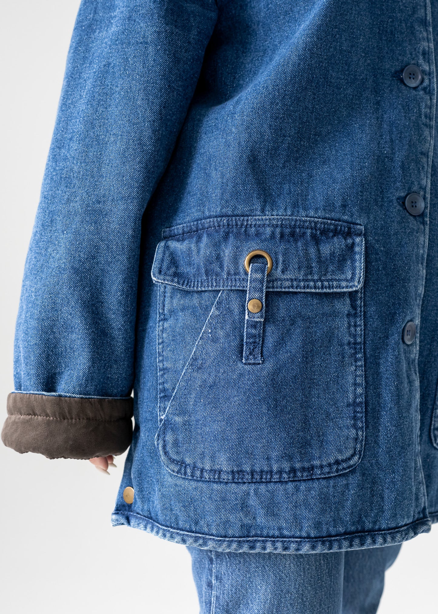 Close-up of a vintage blue denim jacket with a pocket and button details on a white background
