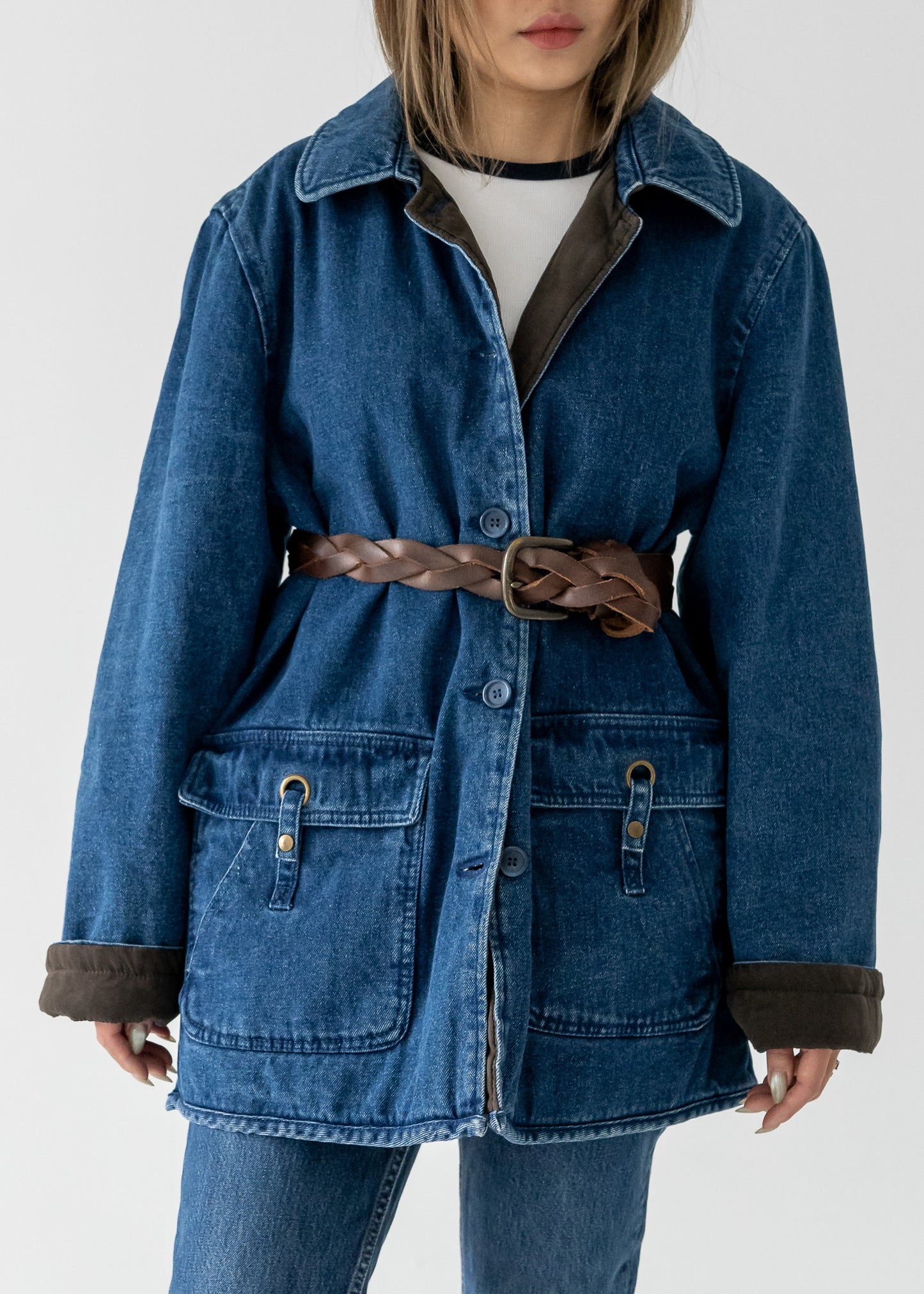Person wearing a blue denim jacket and jeans with a vintage braided leather belt on a white background