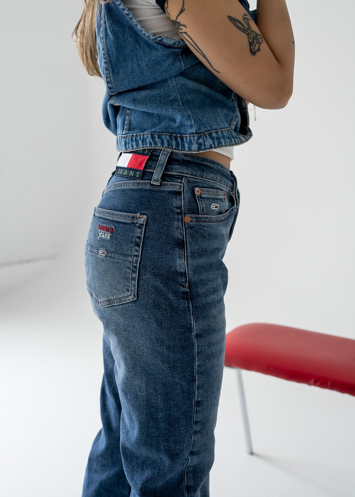 A person viewed from the back wearing vintage high-waisted, straight leg medium wash denim jeans with visible metal button closure and a brand badge on the back pocket.