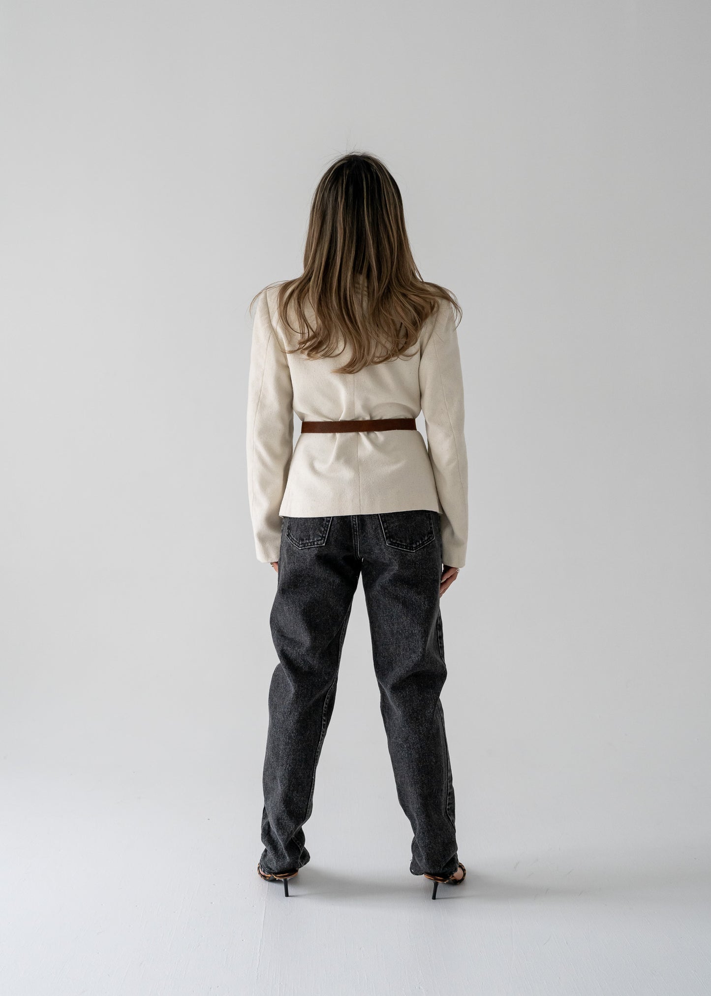Woman standing against a white background wearing straight leg vintage black medium wash high rise jeans and cream linen blazer