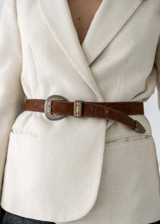 Close-up of a person wearing a beige coat with a brown belt and decorative buckle.