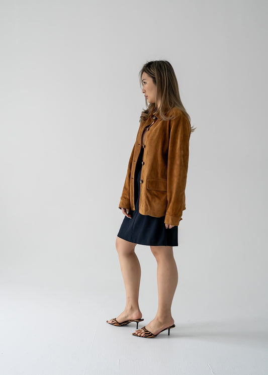 A person wearing a vintage tawny brown suede leather button-up collared jacket with a black mini skirt.