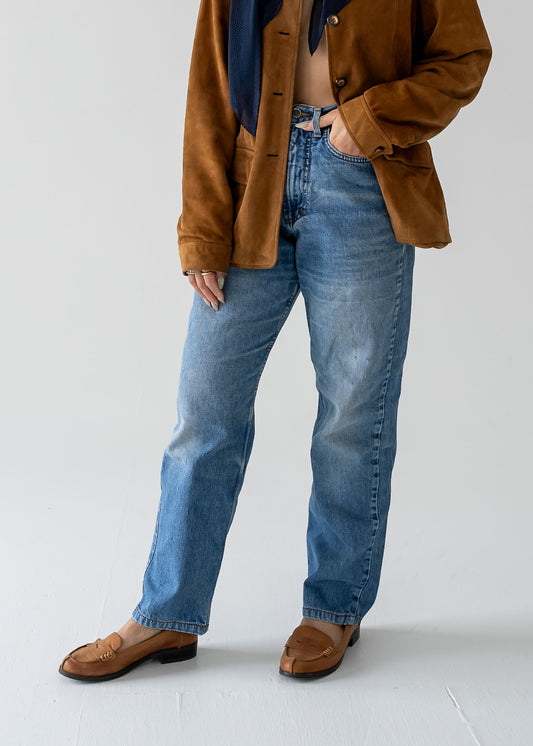 Person wearing vintage blue jeans and a brown suede jacket on a plain background