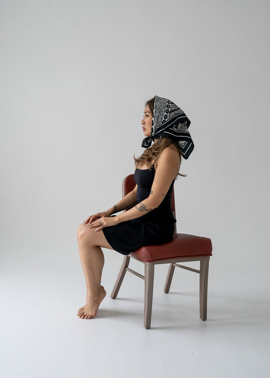Person sitting on a chair wearing a patterned headscarf and vintage fitted A-line mini skirt in black and white stripes against a plain background.