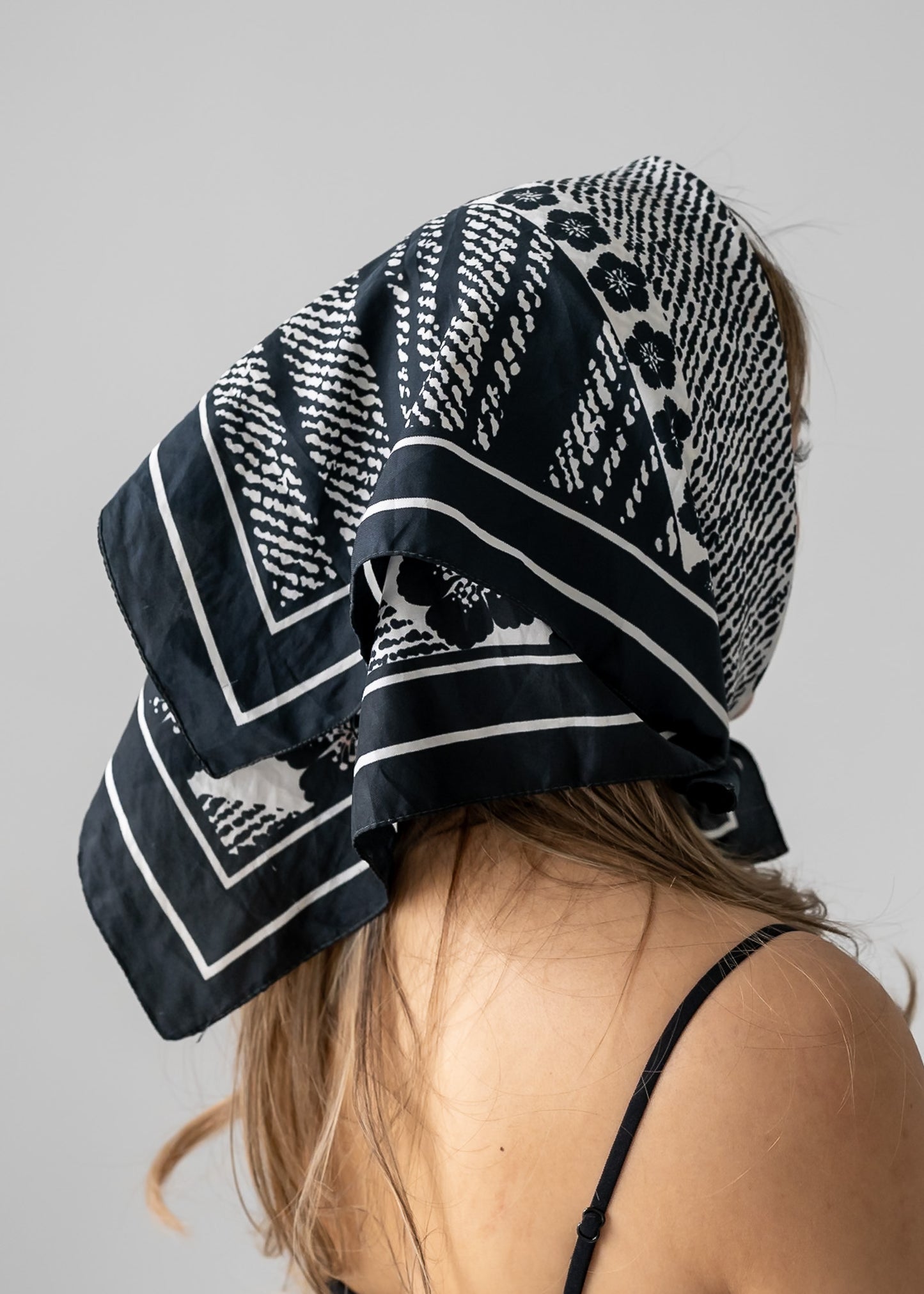 Person wearing a black and white floral and striped patterned headscarf on a plain background