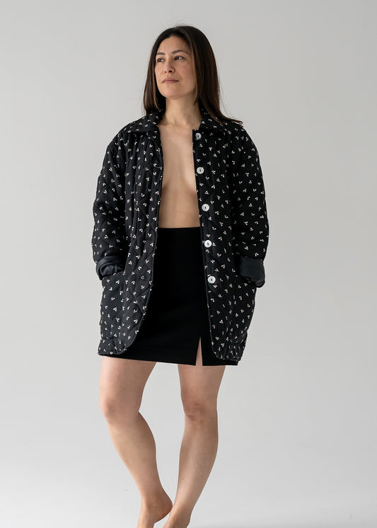 Woman wearing a vintage black and beige small leaf print silk quilted lightweight jacket with long sleeves and a classic collar and black skirt on a plain background