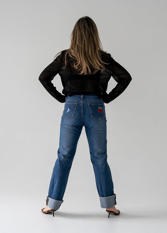 Person wearing vintage medium wash blue jeans with cuffed hem with fruit appliques and a black top from the back.