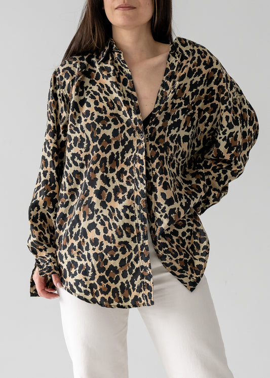 Person wearing a vintage silk leopard animal print long sleeve button up blouse with white pants on a plain background