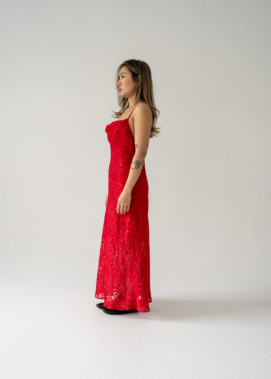 A model wearing a cherry red sheer floral burnout cowl neck thin strap dress with a vertical slit on the left side.