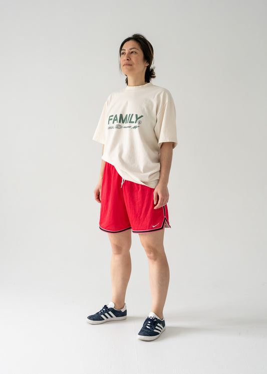 Person wearing a white t-shirt with 'FAMILY' text and vintage red mesh Nike shorts with black side stripes on a plain background.