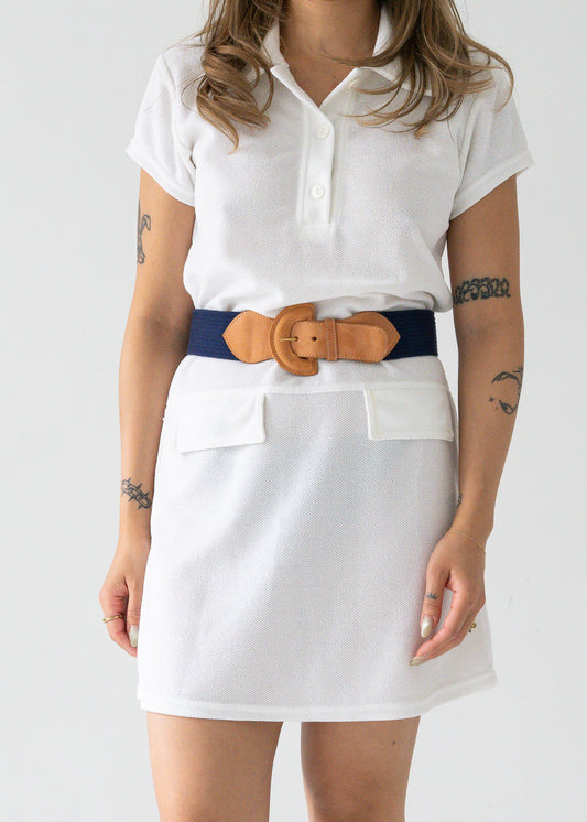 vintage bright white drop waist button up collared short sleeve tennis mini dress with a navy blue and leather belt worn by a person on a plain background