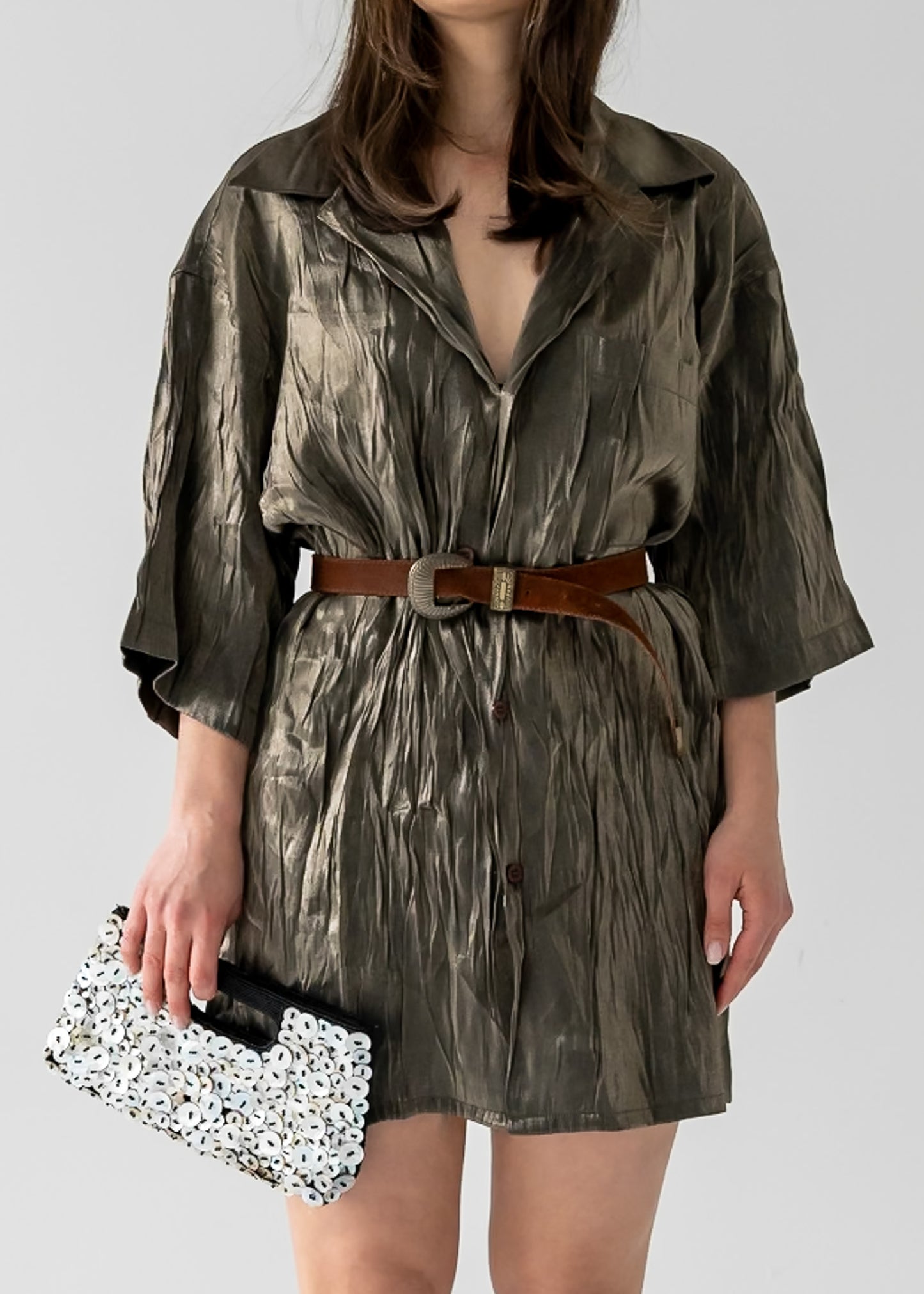 Person wearing a green patterned dress with a brown suede belt with a decorative buckle, holding a black and white shell clutch.