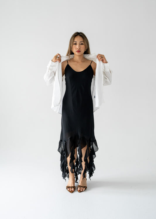 Woman wearing a black dress with a vintage white, long-sleeved, button-up blouse with a mini ruffle at the wrist, on a plain background