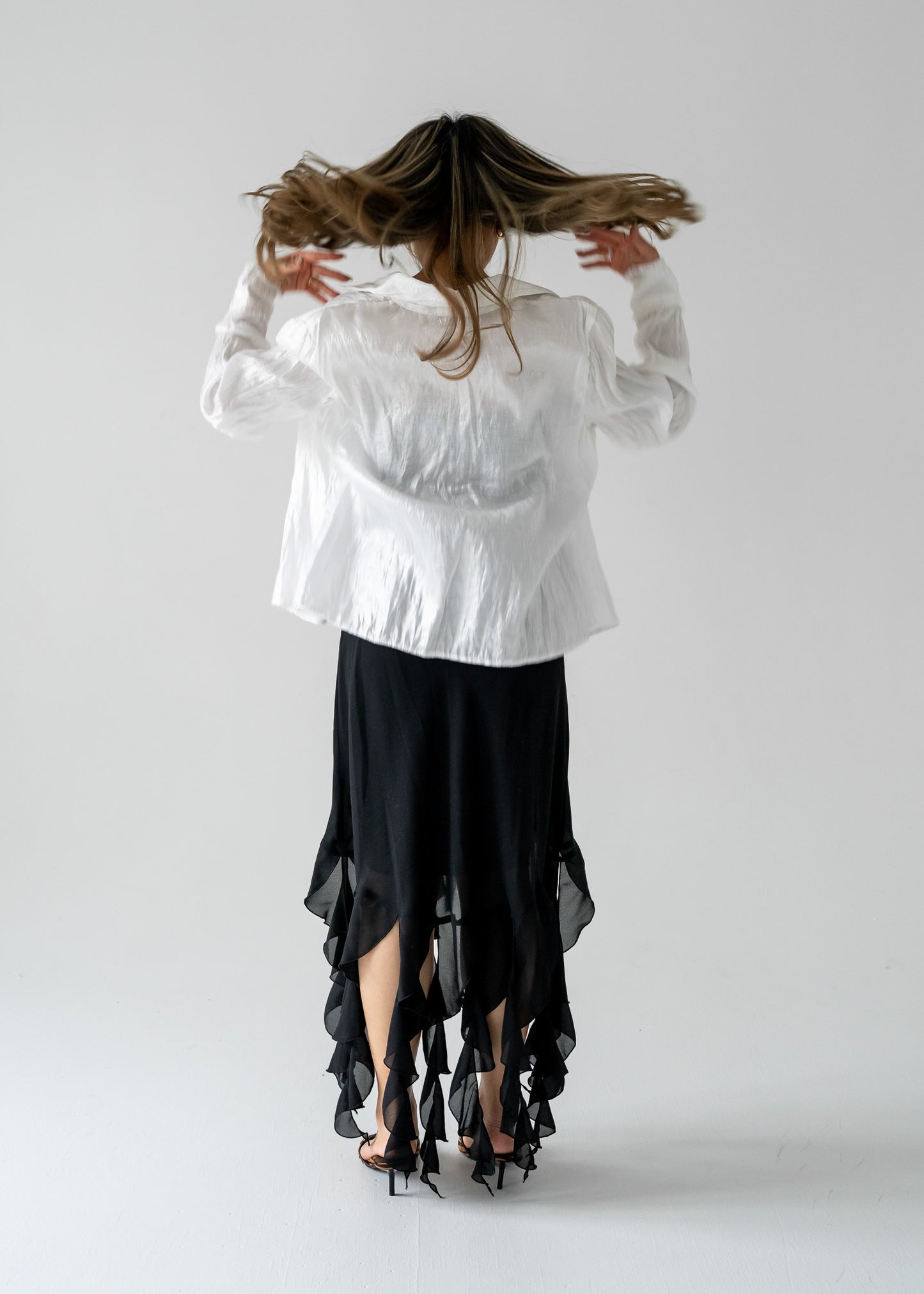 Person wearing a white blouse and black vintage ruffled dress, standing against a plain background.