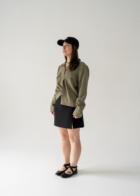 Person wearing a vintage moss green long sleeve button up shacket and black skirt on a white background
