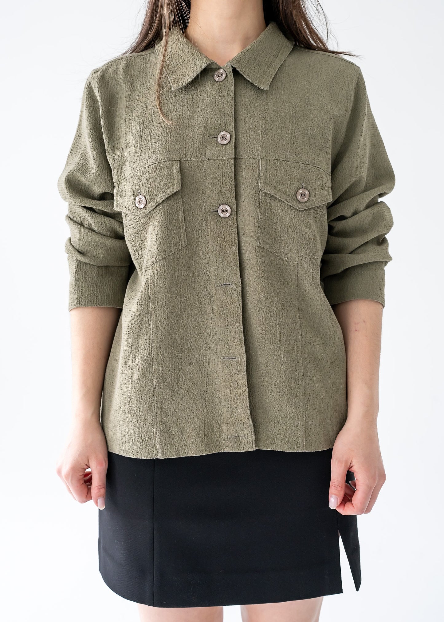 Person wearing an olive vintage moss green long sleeve button up shacket with a white background