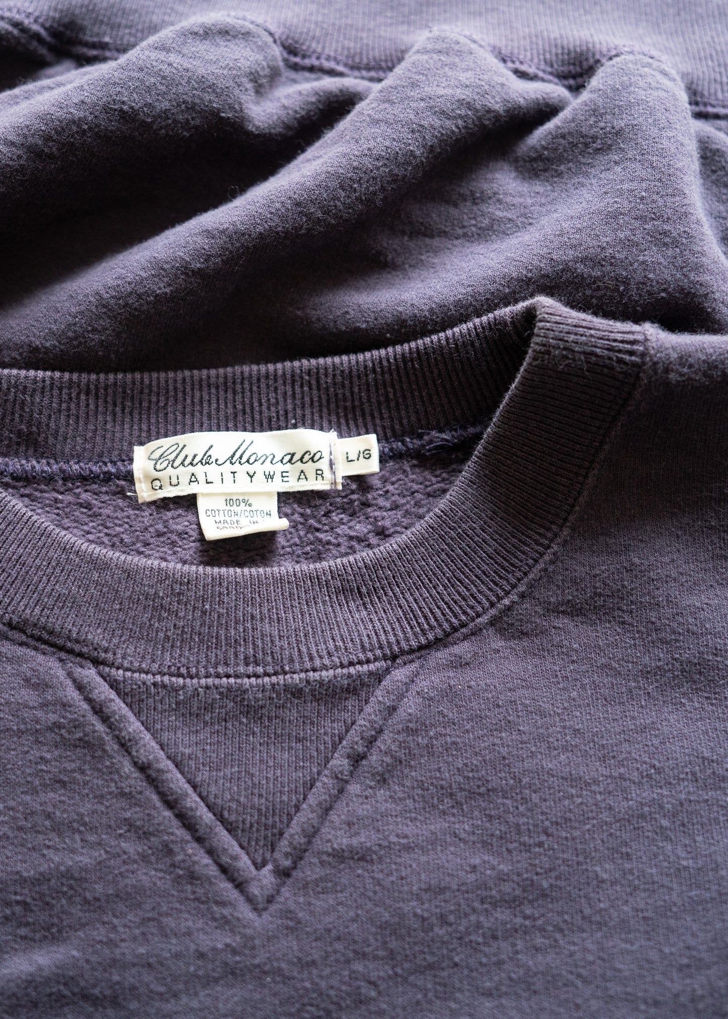 Close-up of a dark purple sweatshirt with a vintage Club Monaco label on the collar.