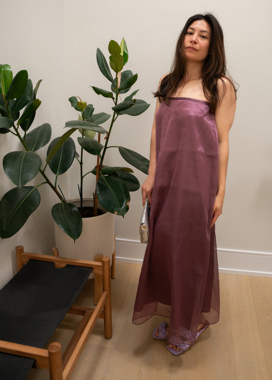 Woman in a strapless mauve purple dress standing in a room with plants and a chair.