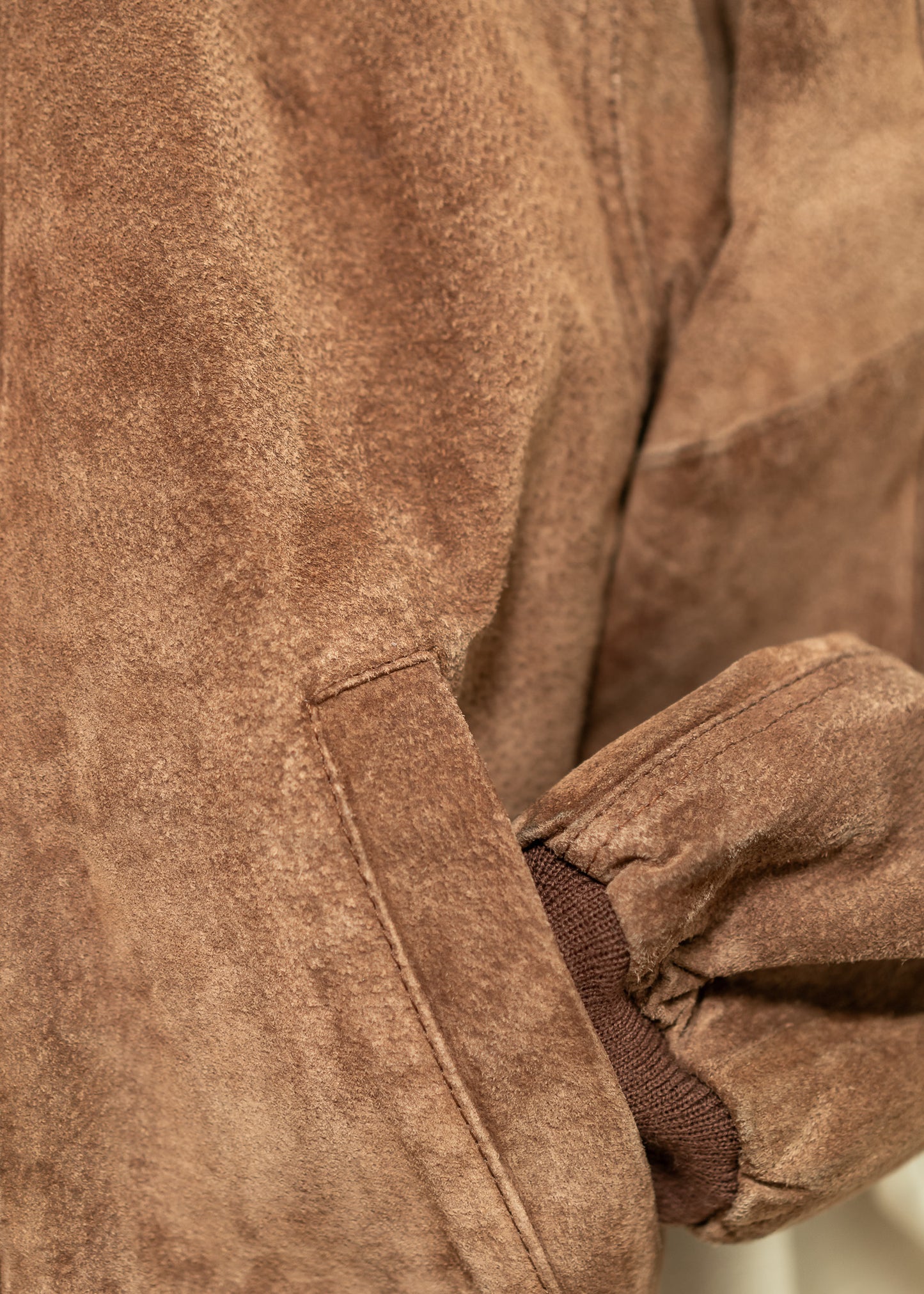 Close-up of a vintage brown suede jacket with a focus on the sleeve and pocket.