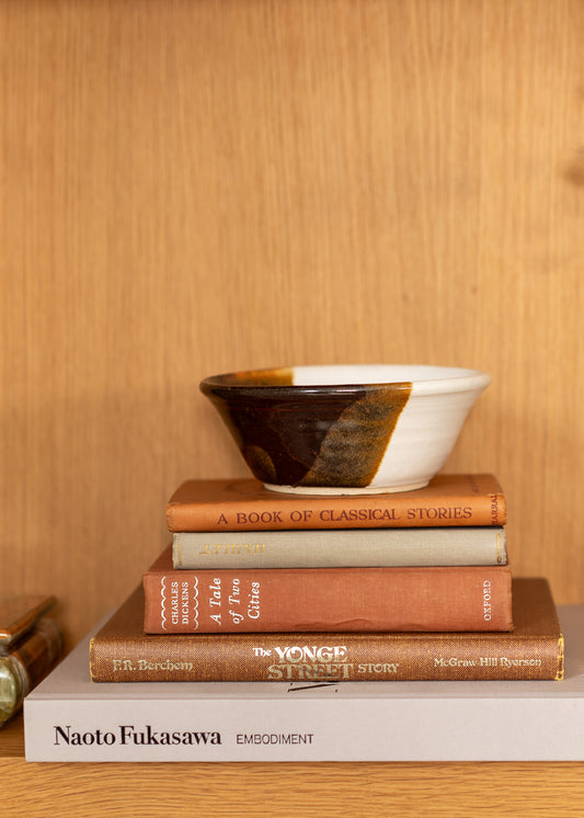 Stack of vintage books with a ceramic bowl on top against a wooden background