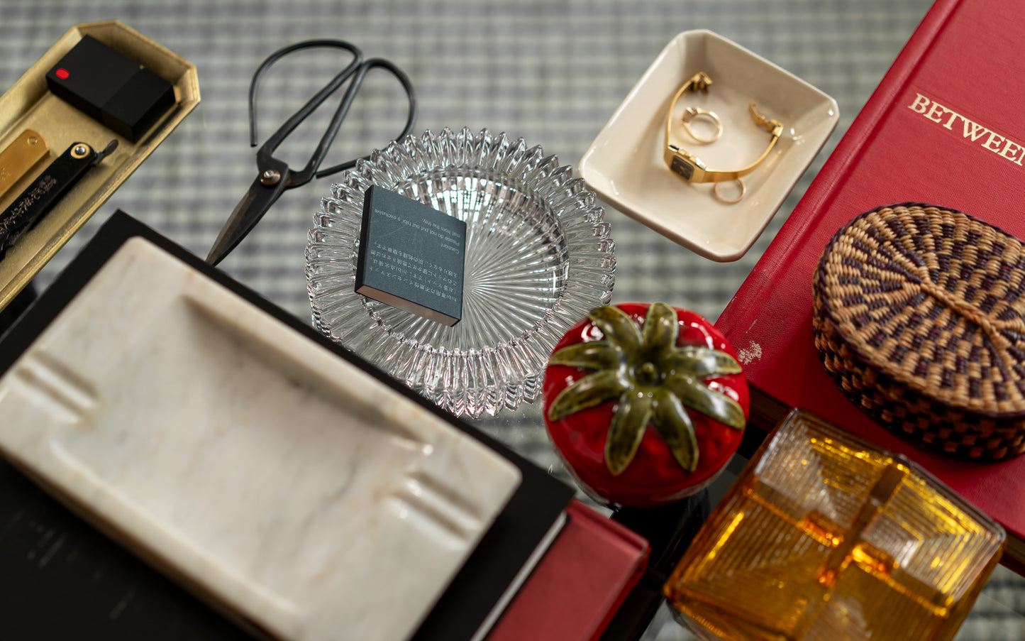 Collection of small vintage items including a woven basket, scissors, a ring, and a small plant on a textured surface.