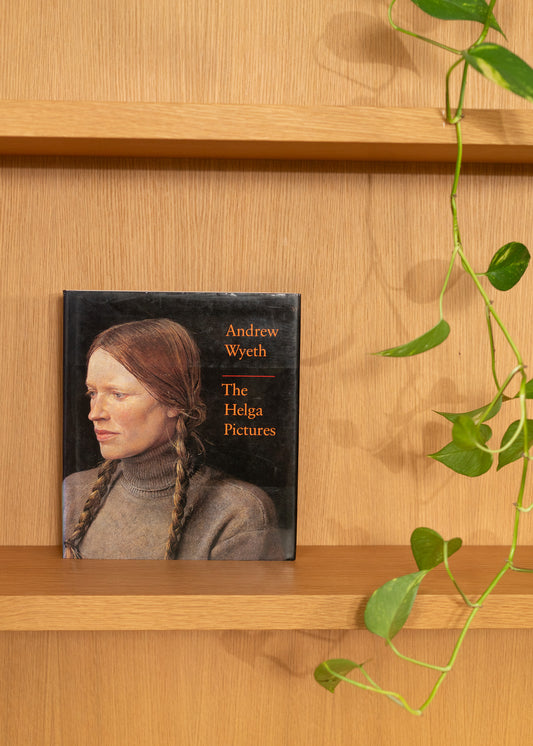 Vintage book titled 'The Helga Pictures' by Andrew Wyeth on a wooden shelf with a plant.