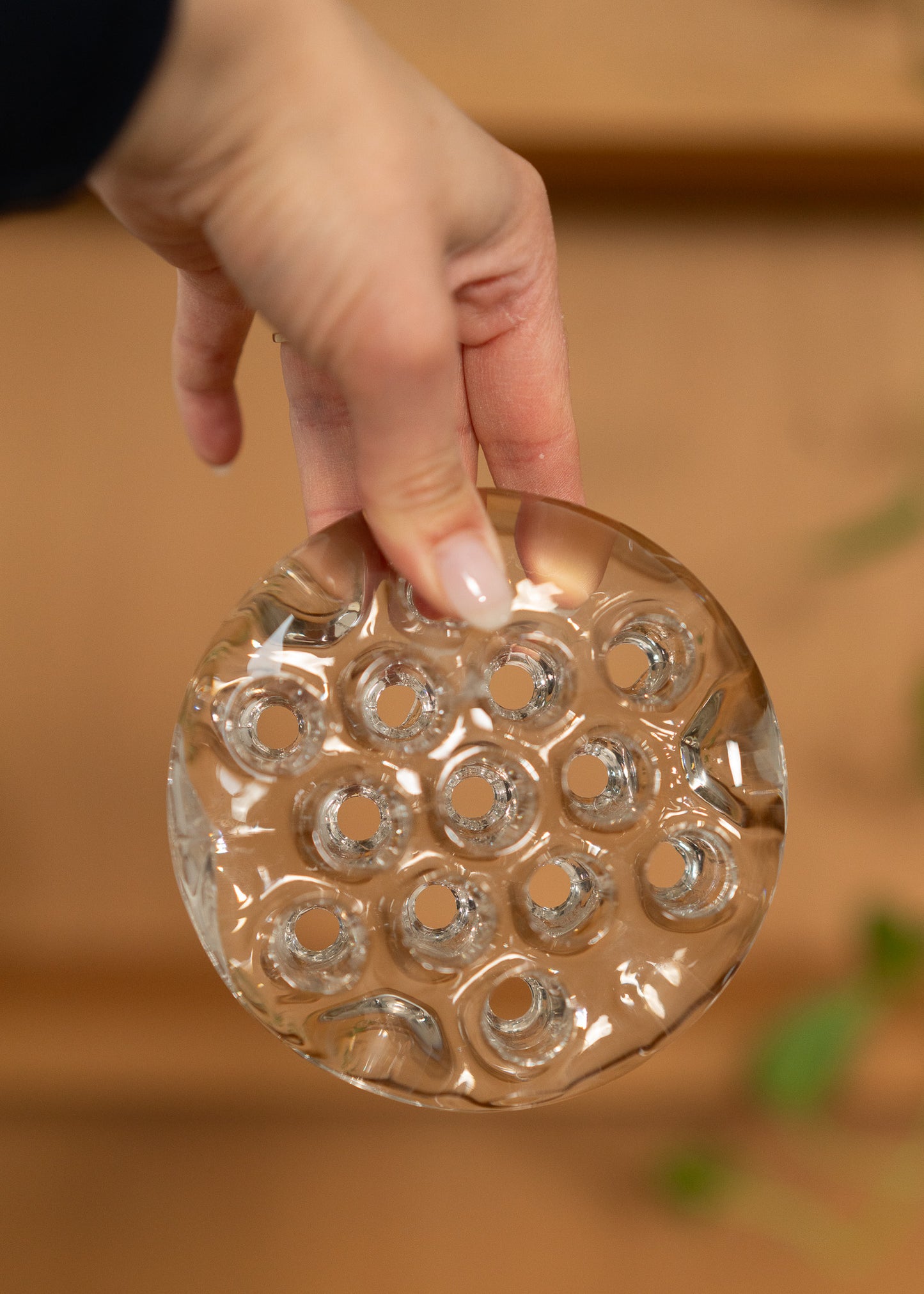 Hand holding a vintage round, clear glass flower frog against a blurred background