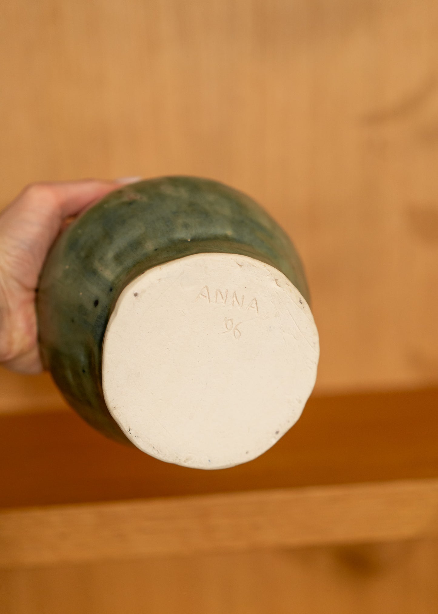 Hand holding a vintage green ceramic jar with a white lid against a wooden background