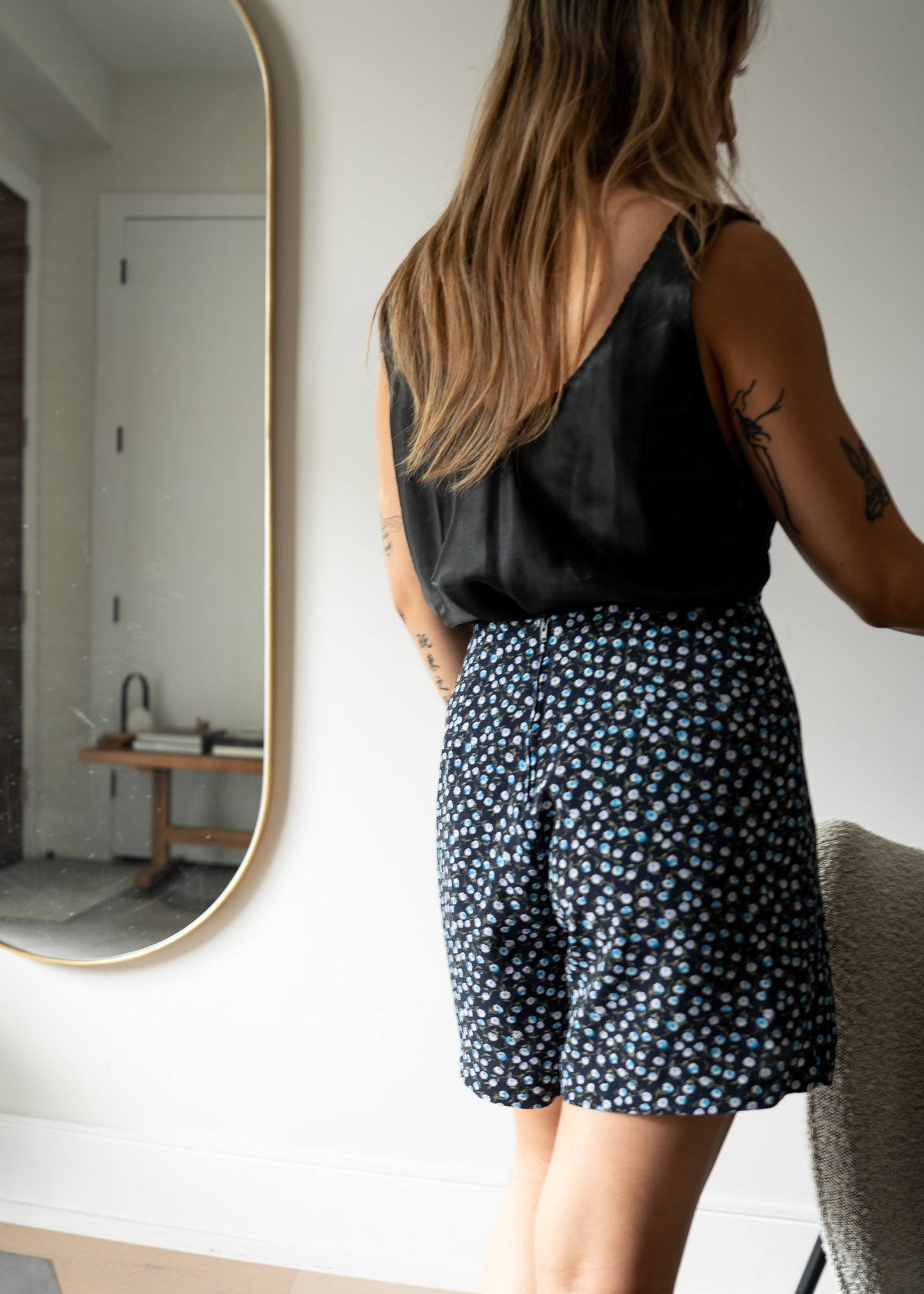 Person wearing a vintage black sleeveless top and floral shorts standing in front of a mirror.