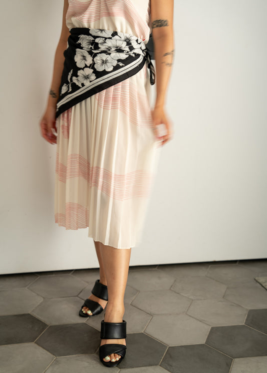 Woman wearing a white and pink pleated dress with a black floral scarf around her waist against a white background