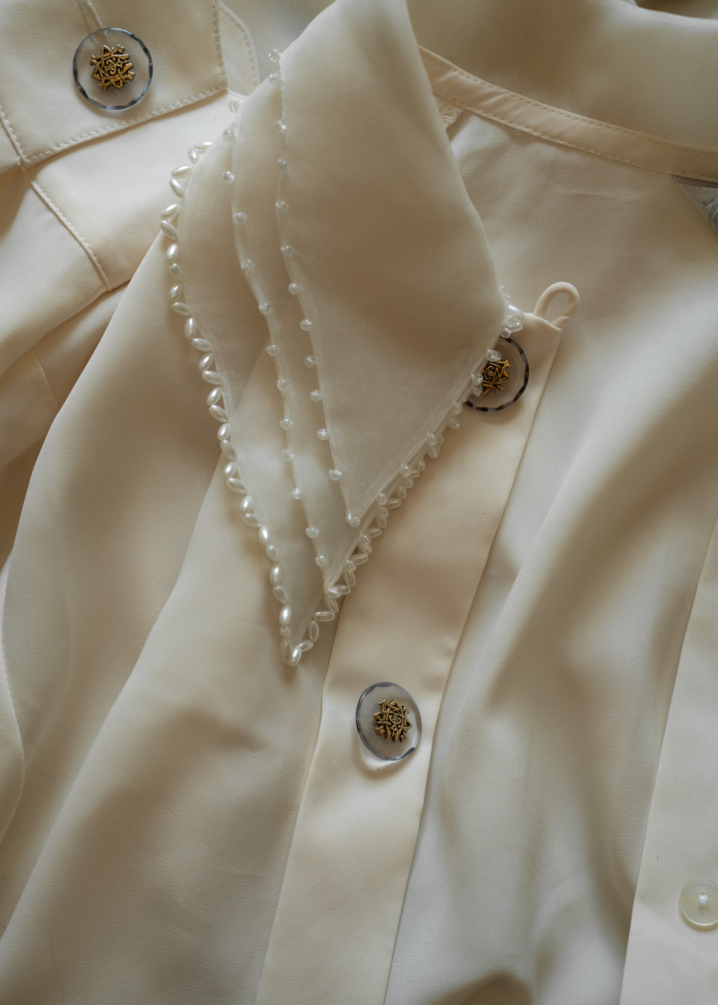 Close-up of a cream-colored blouse with beaded pearl details on collar and decorative buttons.