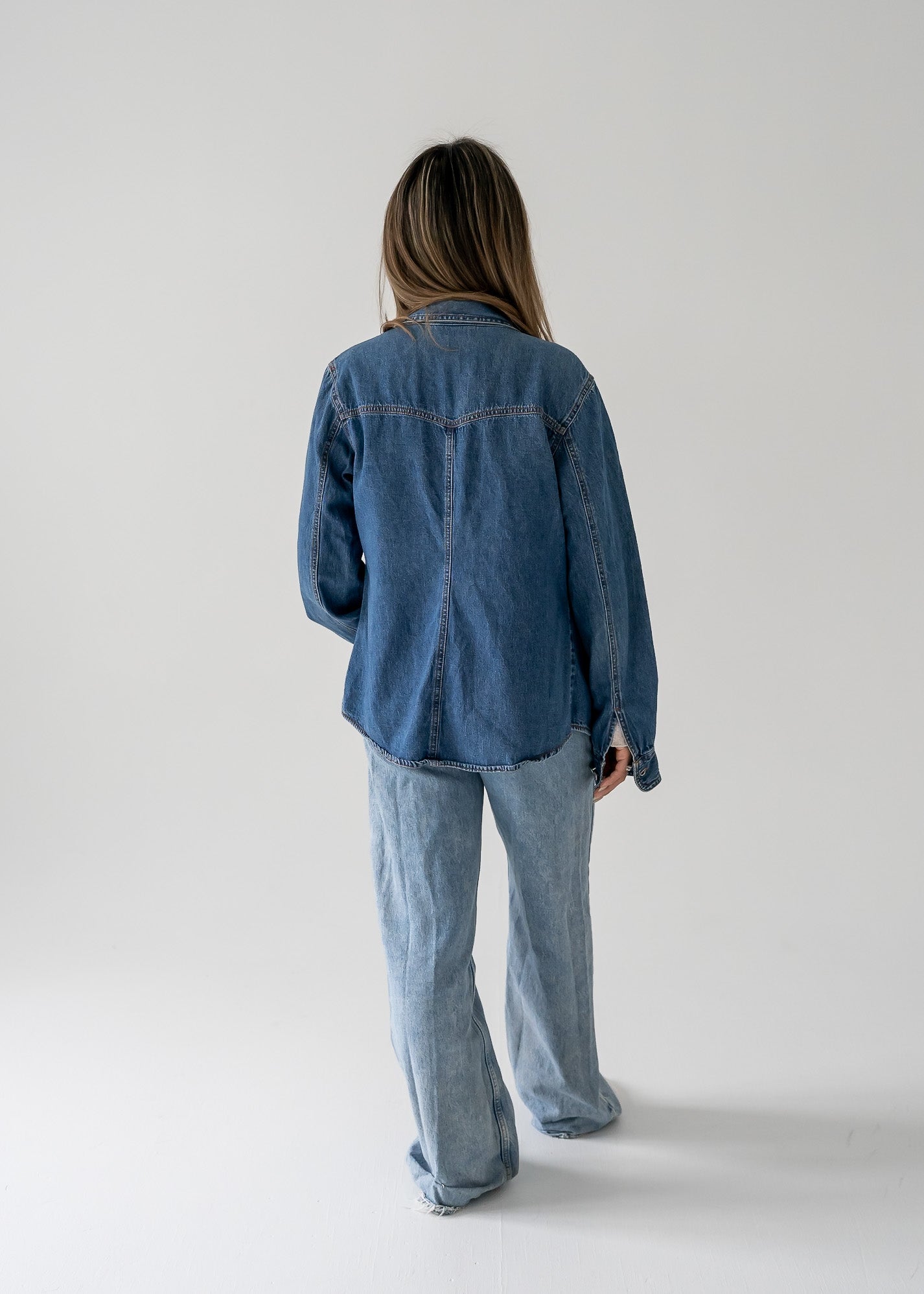 Person wearing a vintage medium wash denim button up long sleeve shirt and jeans on a white background