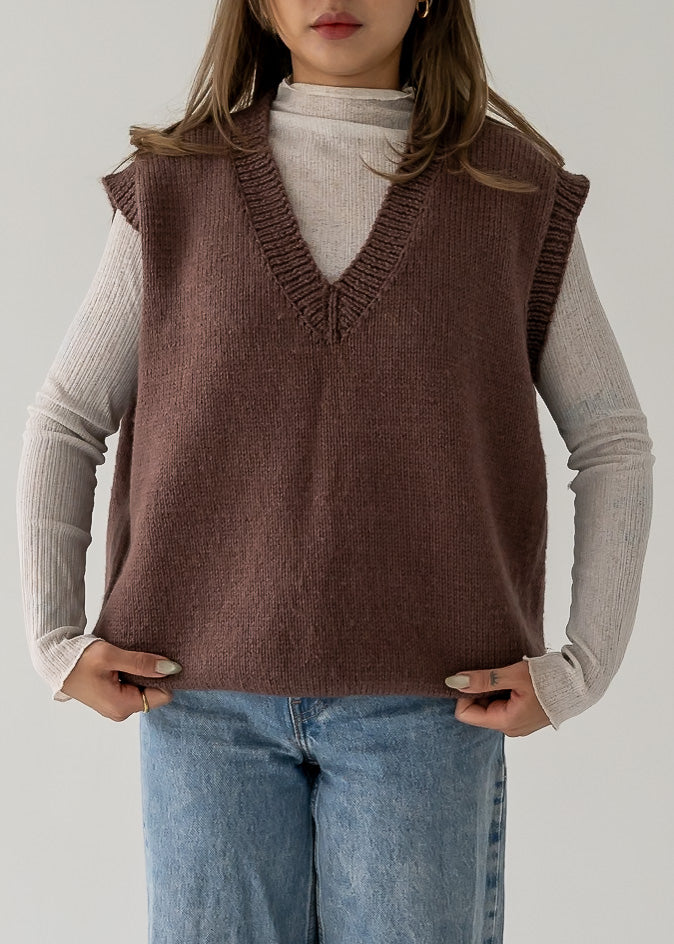 Person wearing a warm vintage brown thick knit V neck vest over a beige turtleneck and blue jeans.