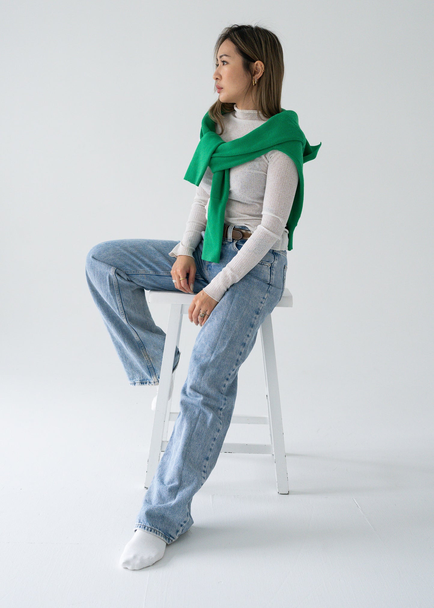 Person sitting on a stool wearing a vintage bright parakeet green open collar knit long sleeve pullover sweater and blue jeans.