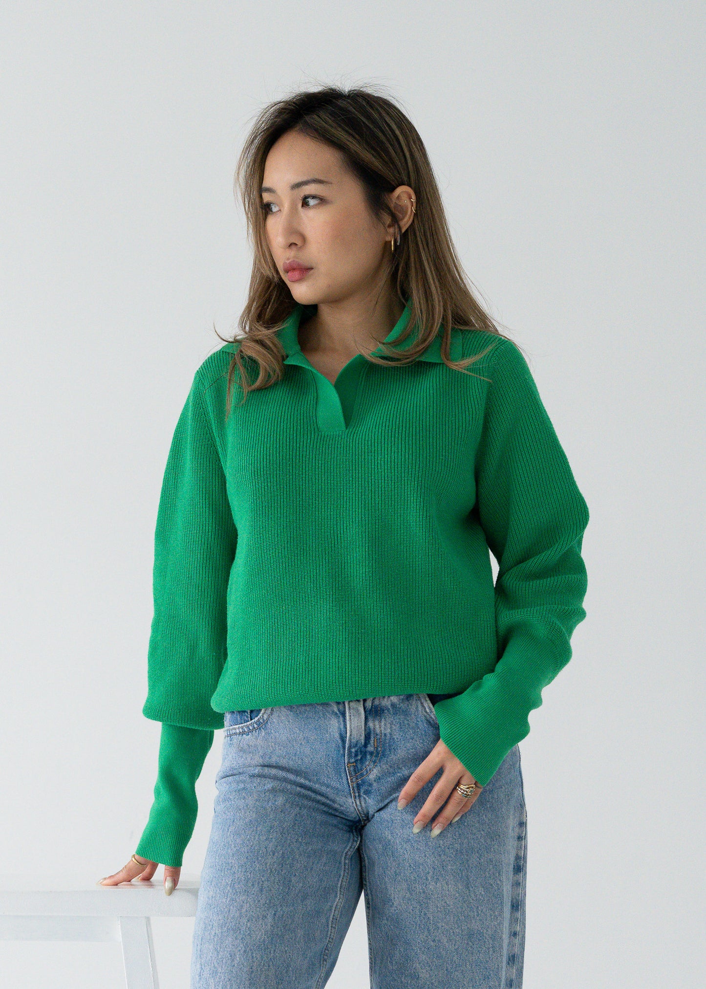 Person wearing a vintage bright parakeet green open collar knit long sleeve pullover sweater and blue jeans against a plain background