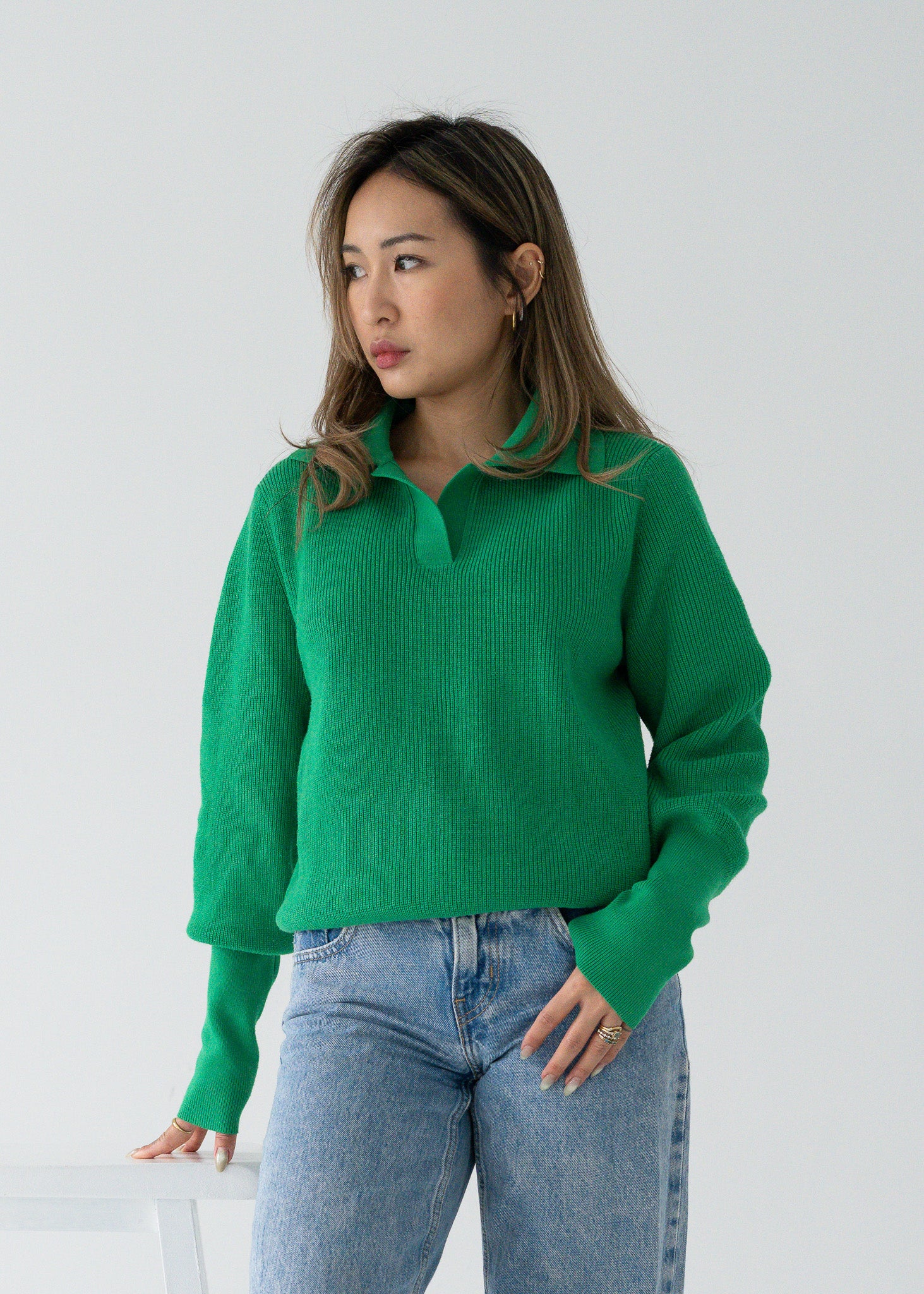 Person wearing a vintage bright parakeet green open collar knit long sleeve pullover sweater and blue jeans against a plain background