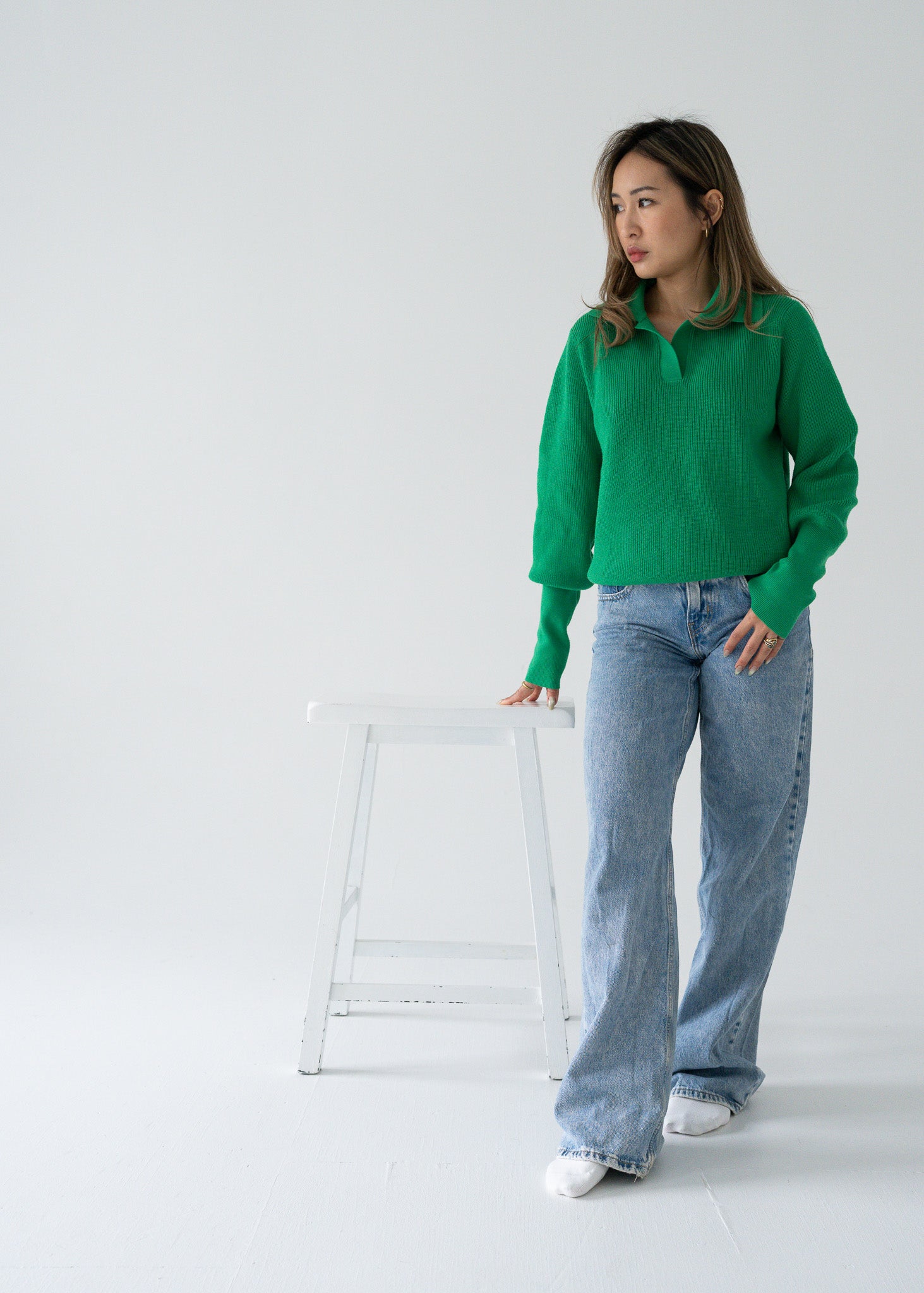 A person wearing a vintage bright parakeet green open collar knit long sleeve pullover sweater in a studio setting with a light-colored background.