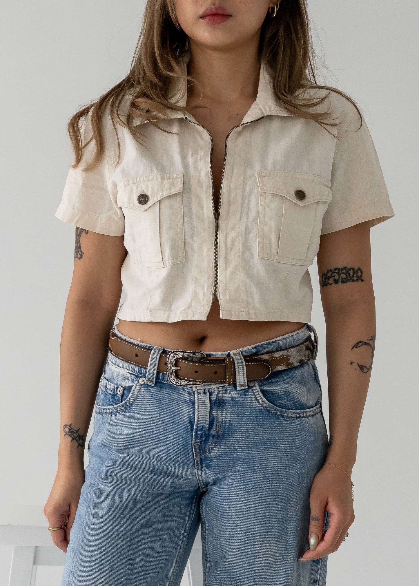 Person wearing a vintage beige cropped linen zip-up collared short sleeve jacket style top and blue jeans.