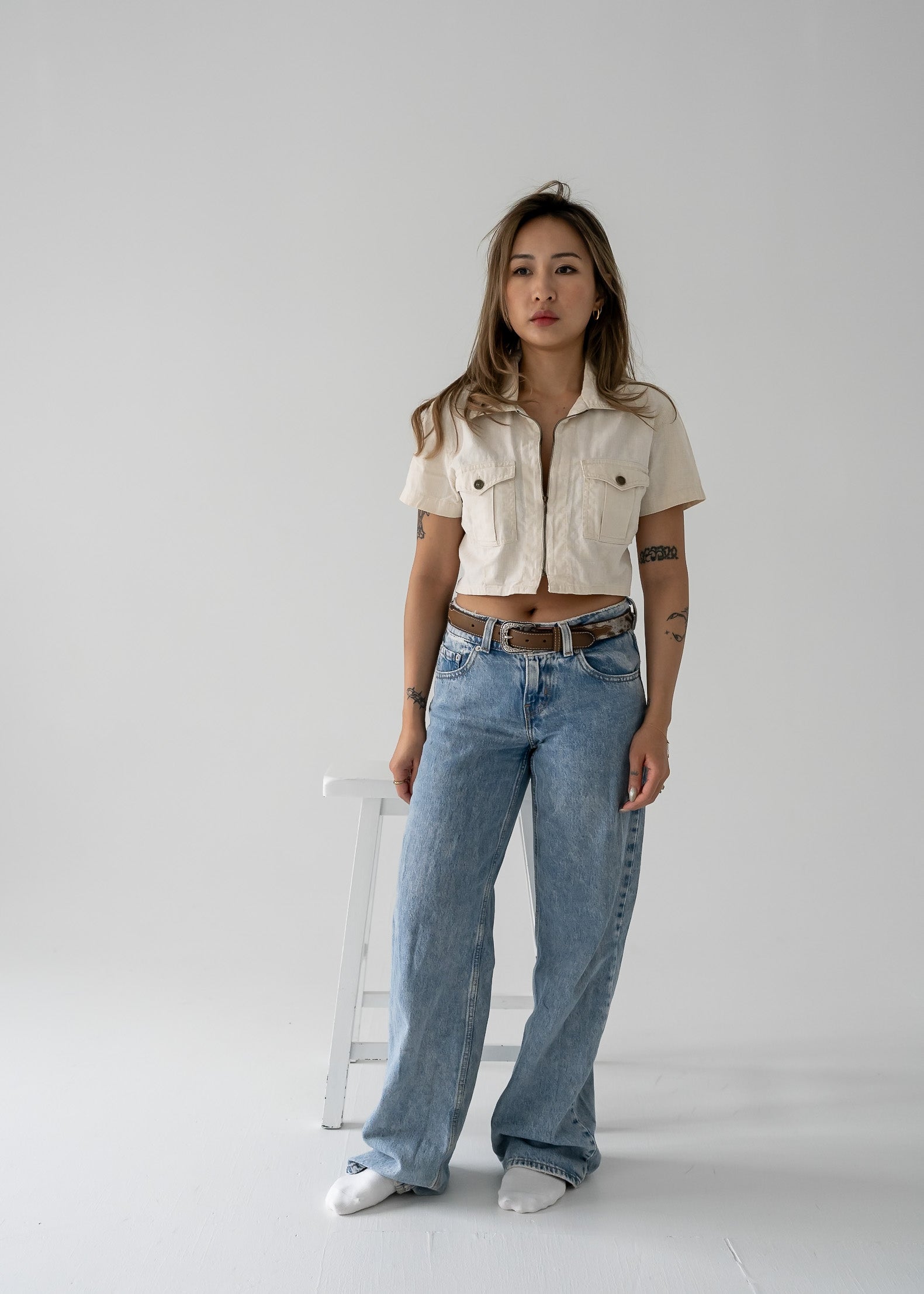 woman wearing a vintage beige cropped linen zip-up collared short sleeve jacket style top and blue jeans