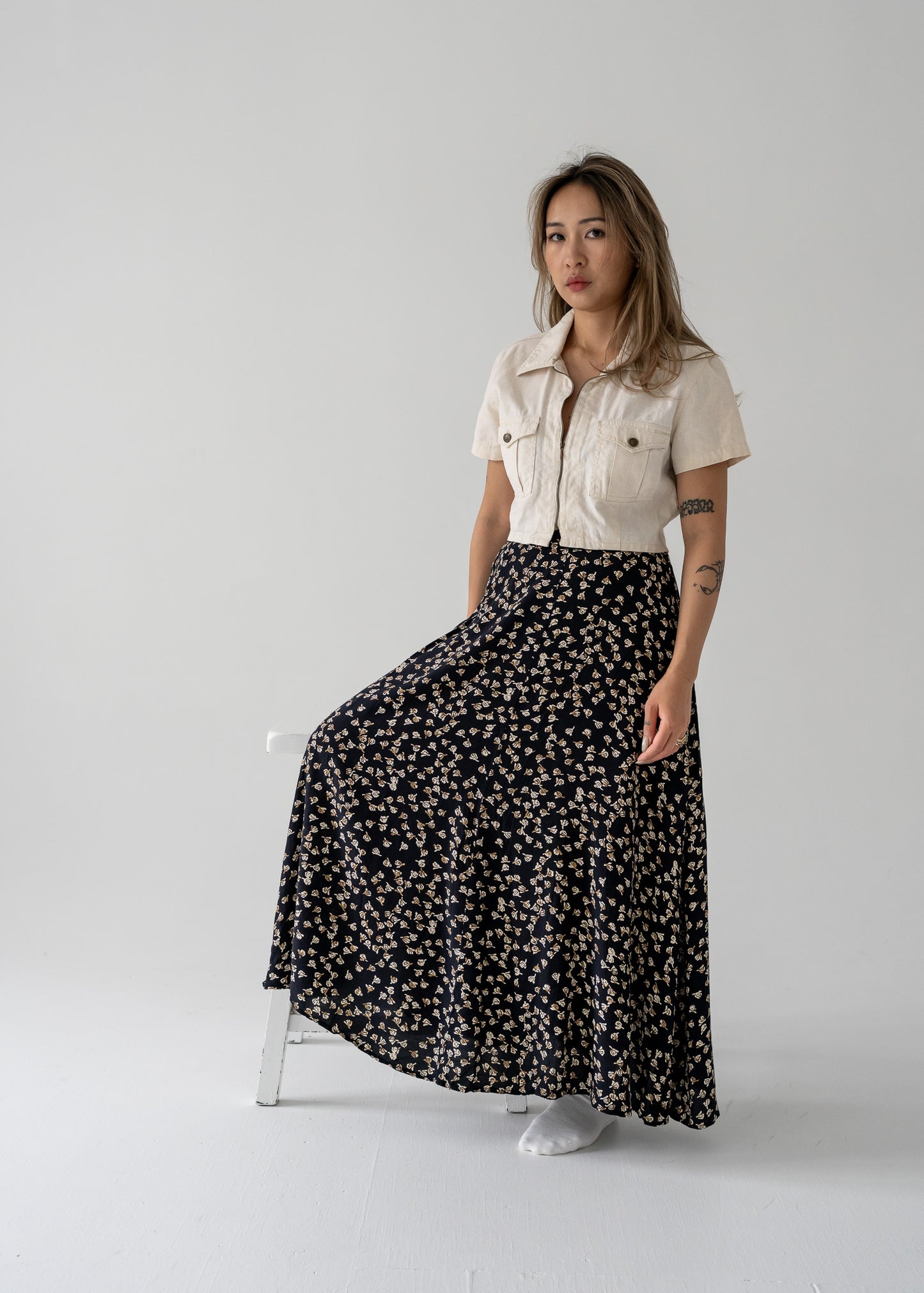 A model wearing a vintage flowy midi skirt with a floral pattern, paired with a beige shirt.