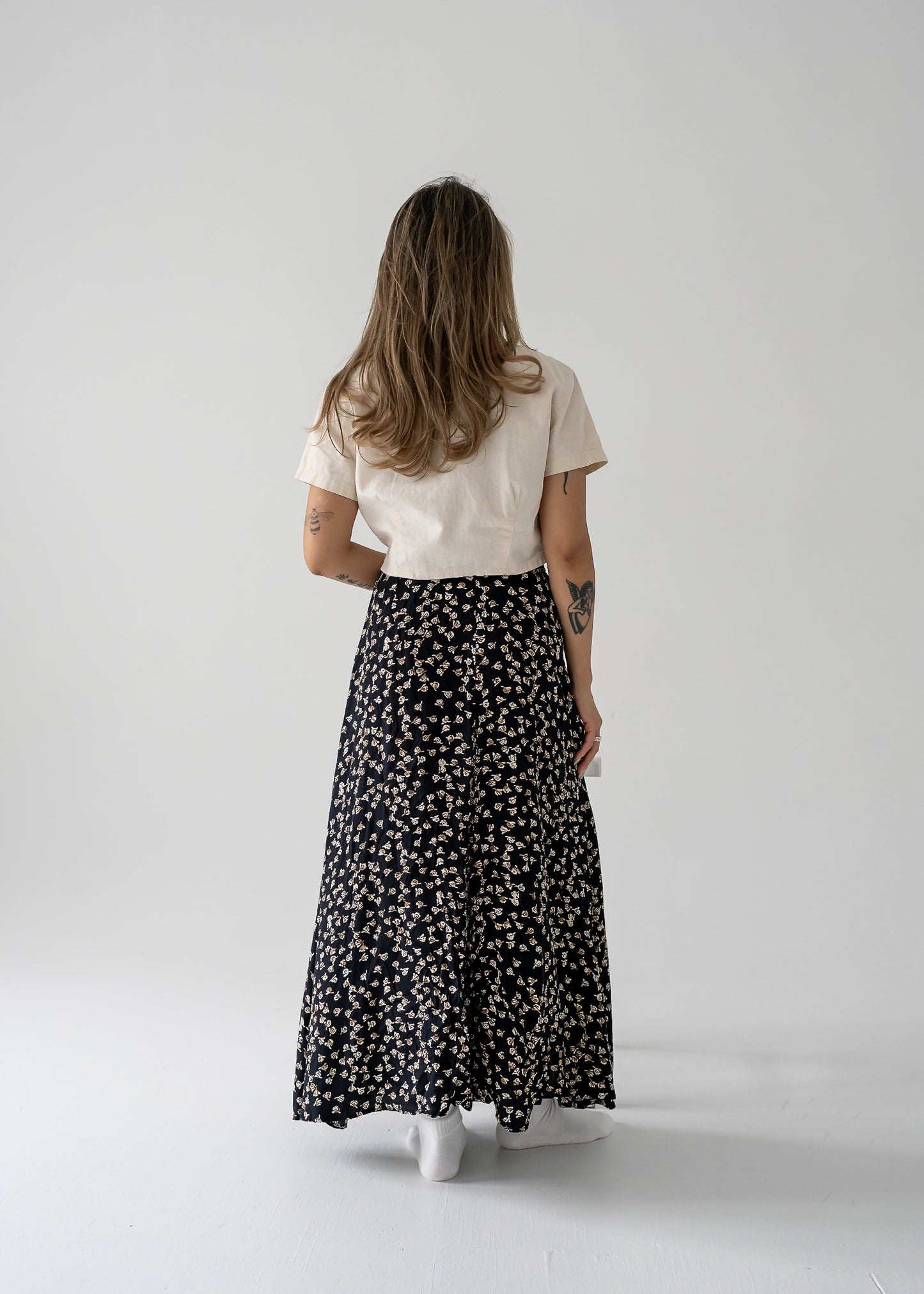 A person viewed from the back wearing a vintage flowy midi skirt with a small black and brown floral print, paired with a cream-colored top.