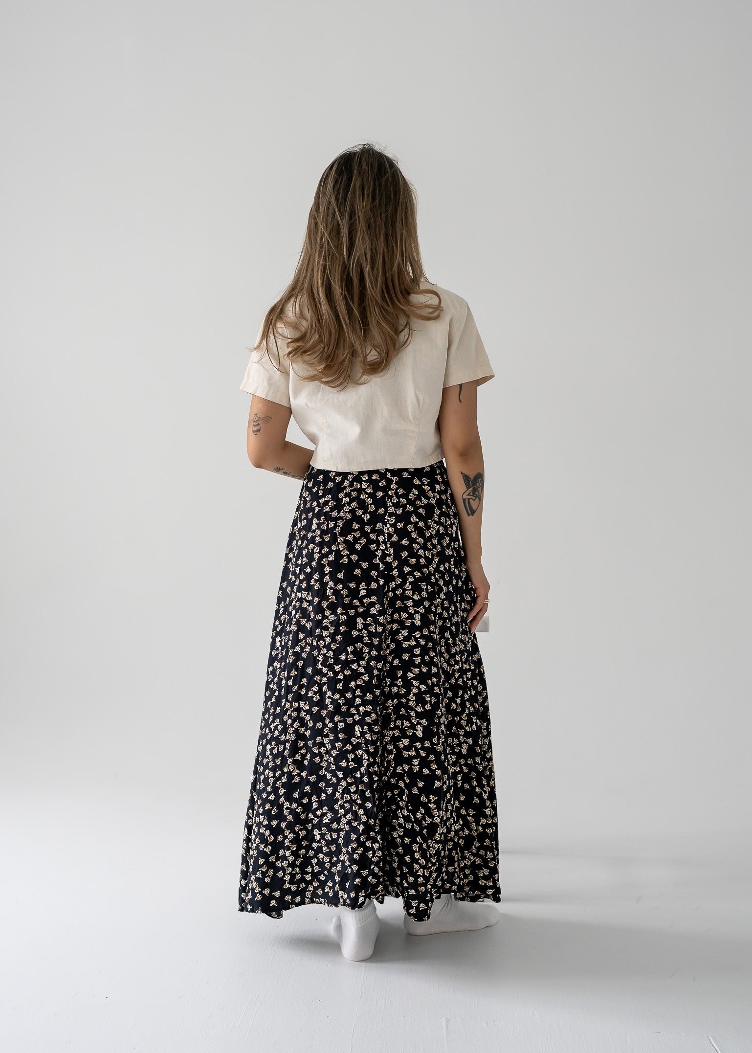 A person viewed from the back wearing a vintage flowy midi skirt with a small black and brown floral print, paired with a cream-colored top.
